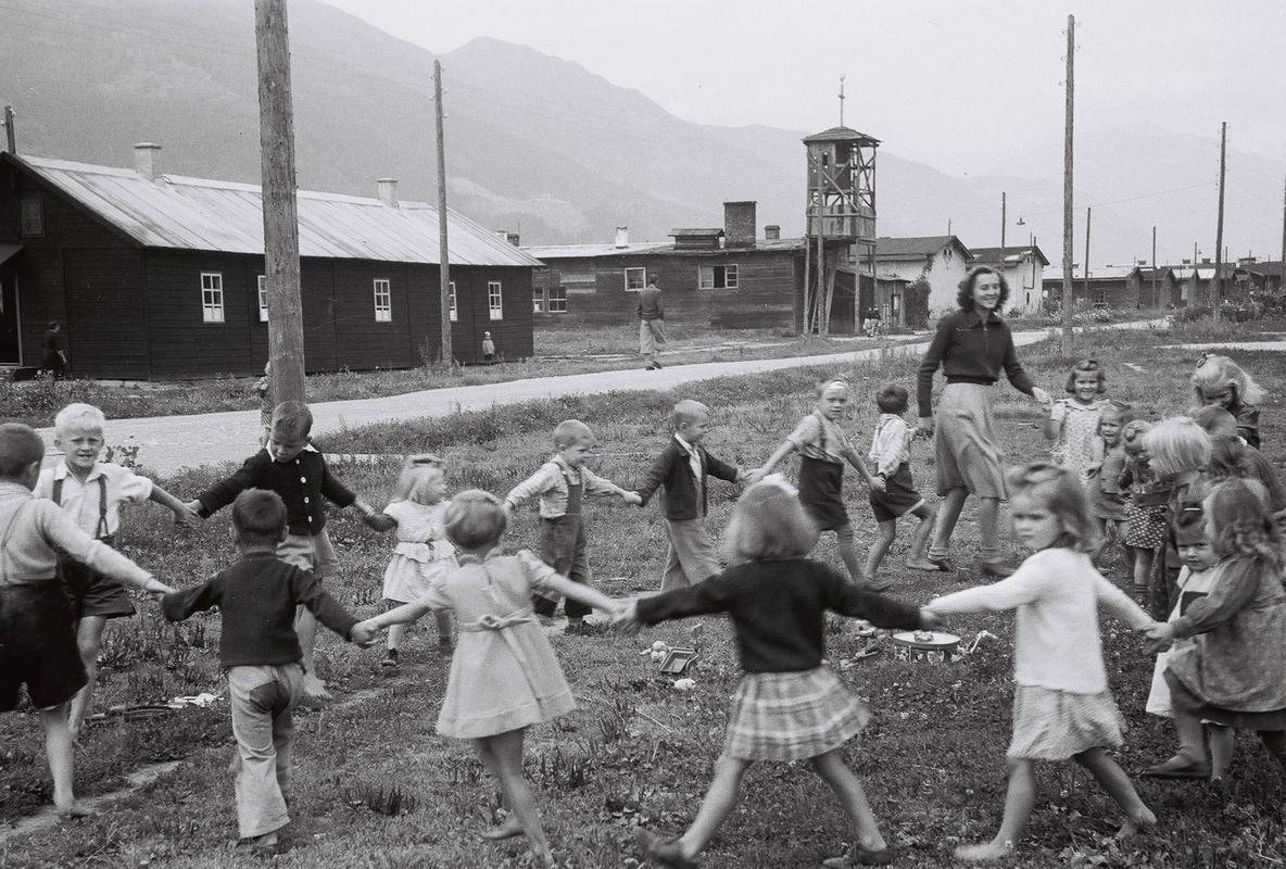 Spittal leta 1952: Mladinski dom s cerkvenim zvonikom v ozadju, z otroki pa pleše vzgojiteljica Pavla Žukovec. Foto: MNZS