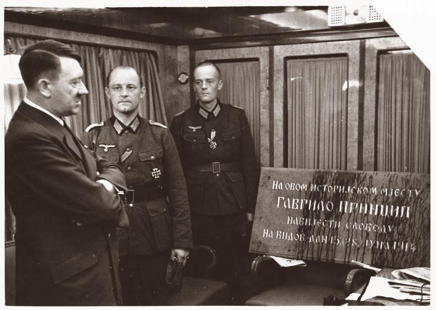 Adolf Hitler si ogleduje spominsko ploščo, posvečeno Gavrilu Principu, atentatorju na avstro-ogrskega prestolonaslednika Franca Ferdinanda, kar je bil povod za izbruh prve svetovne vojne. Ob 52. rojstnem dnevu 20. aprila 1941 so mu jo kot darilo poslale nemške enote, ki so ravnokar zasedle Kraljevino Jugoslavijo. Fotografijo je v poveljniškem vlaku 