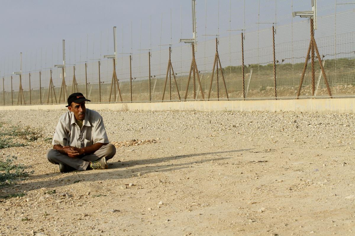 Palestinski kmet med čakanjem na vojaka, da odpre vrata v ograji. Palestincem je dostop do njihove zemlje onkraj zidu oziroma ograje dostopen le z dovoljenjem izraelske vojske, ki pa ga zelo težko in redko dobijo. Ob tem jim vojska pogosto ne da dovoljenja za vnos potrebnega orodja ali materiala za obdelavo zemlje. Foto: EPA