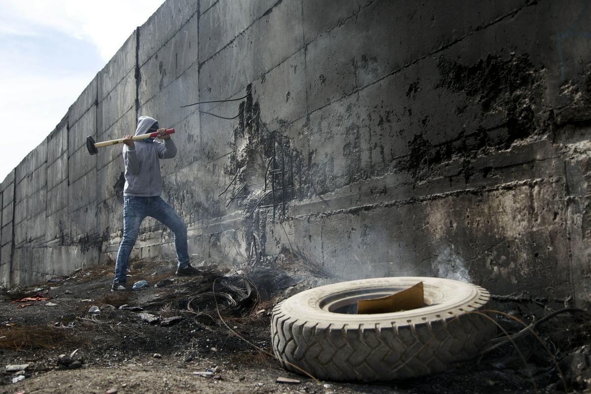 Palestinec med poskusom rušenja zidu. Meddržavno sodišče v Haagu je v svetovalnem mnenju leta 2004 sporočilo, da mora Izrael prenehati graditi na zasedenem ozemlju in tam že zgrajene dele odstraniti, prizadetim pa povrniti škodo. Odločitev sodišča Izraelu ni preprečila nadaljevanja gradnje zidu. Foto: AP