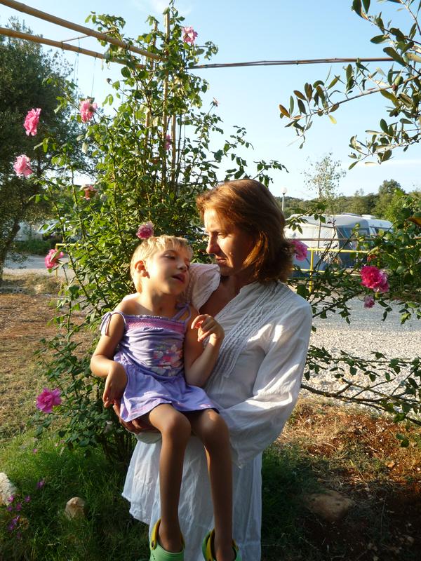 Na fotografiji Spomenka Valušnik v naročju drži hčerkico Najo. V ozadju je grmovje z rožnatimi cvetovi vrtnice. Foto: osebni arhiv