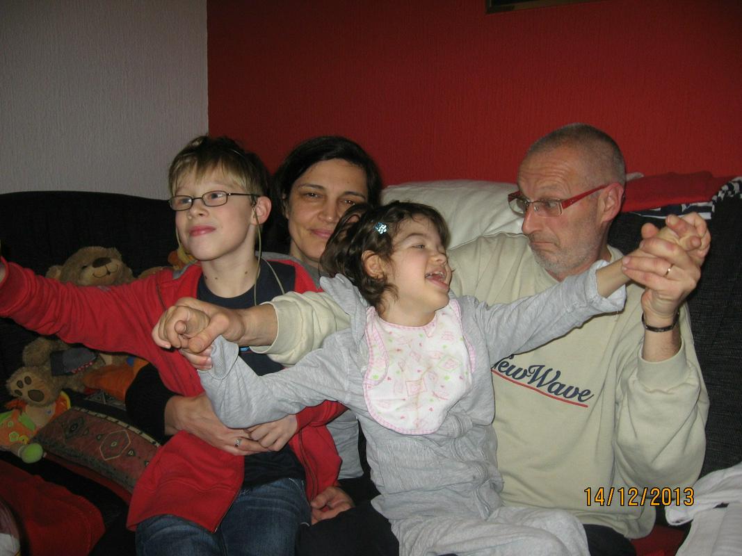 Opis fotografije: Na fotografiji je družina dr. Jasne Murgel. Sedijo na kavču, na levi strani je sin Nik, za njim sedi mama Jasna, v očkovem naročju na desni strani pa sedi hčerka Lea. Foto: osebni arhiv družine Murgel