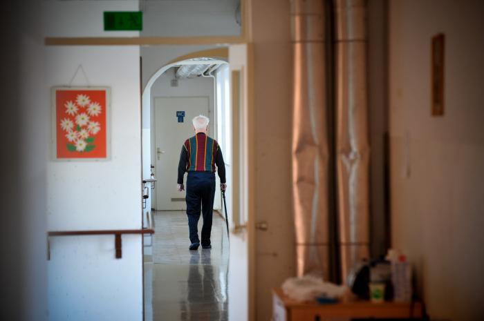 Na fotografiji je starejši moški, ki hodi po hodniku in se opira na palico. Foto: MMC RTV SLO
