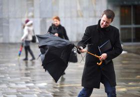 Na fotografiji moški v črnem plašču, ki se upira vetru in dežju. Dežnik drži v roki, a mu ga je močan veter obrnil. V ozadju še dve osebi, ki se s telesom upirata vetru in dežju. Foto: BoBo/ Borut Živulović