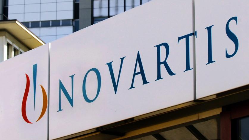 Na fotografiji je velikanski napis NOVARTIS, v ozadju poslovne stavbe z zastekljenim pročeljem. Foto: EPA