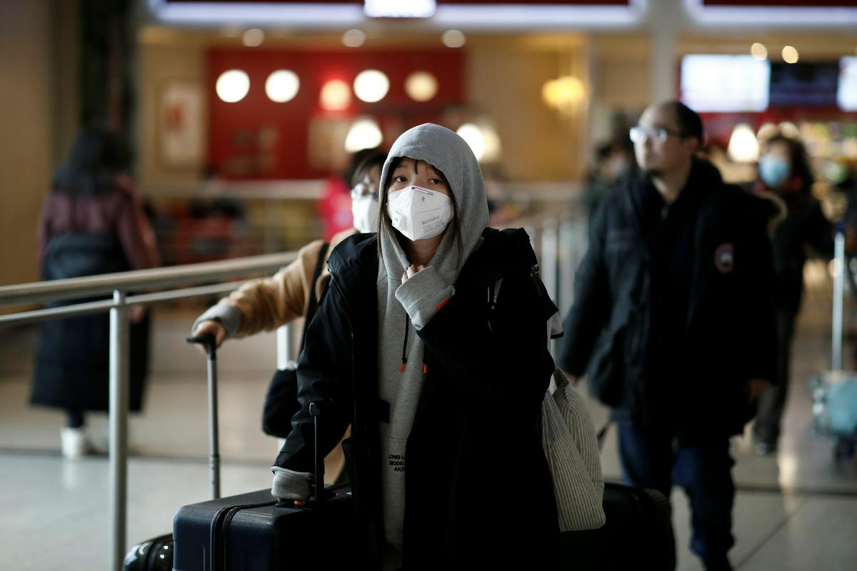 Prebivalci Kitajske potujejo. V rokah imajo kovčke. Ženska v ospredju ima na glavi belo zaščitno masko. Foto: Reuters