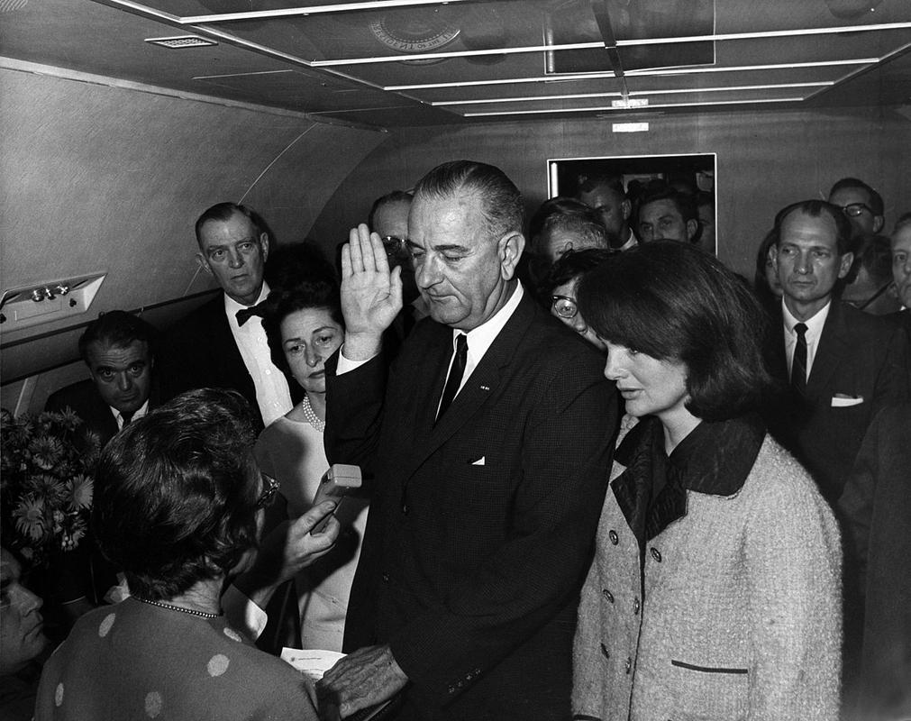 Ikonična fotografija: nekaj več kot dve uri po atentatu na Johna F. Kennedyja je v predsedniškem letalu kot novi predsednik ZDA prisegel Lyndon B. Johnson. Desno ob njem je žena umorjenega Kennedyja Jacqueline Kennedy, skupno se je v letalo ob prisegi stlačilo 27 ljudi. Tik po prisegi je potem letalo iz Dallasa poletelo v Washington. Foto: Wikipedia