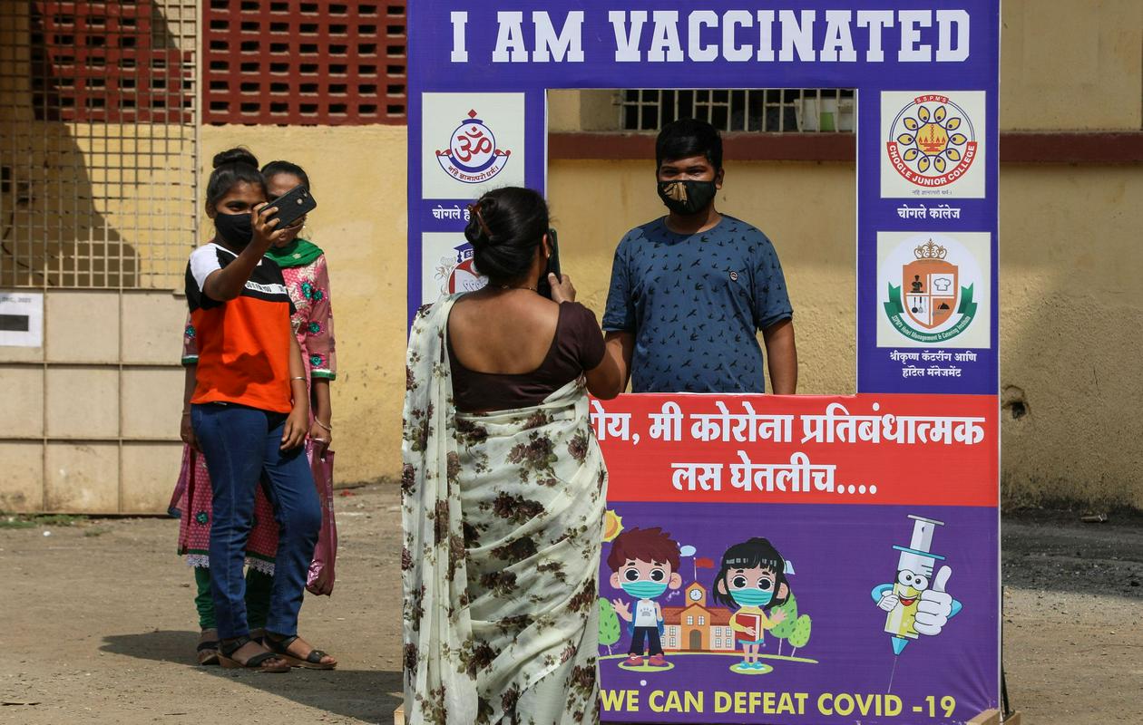 Deček, ki je bil cepljen proti covidu-19 v Indiji, stoji za kartonasto inštalacijo, na kateri piše: 