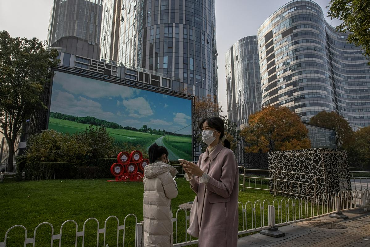 Sprehajalci pred panojem v Pekingu, ki prikazuje zeleno polje in modro nebo. Foto: EPA