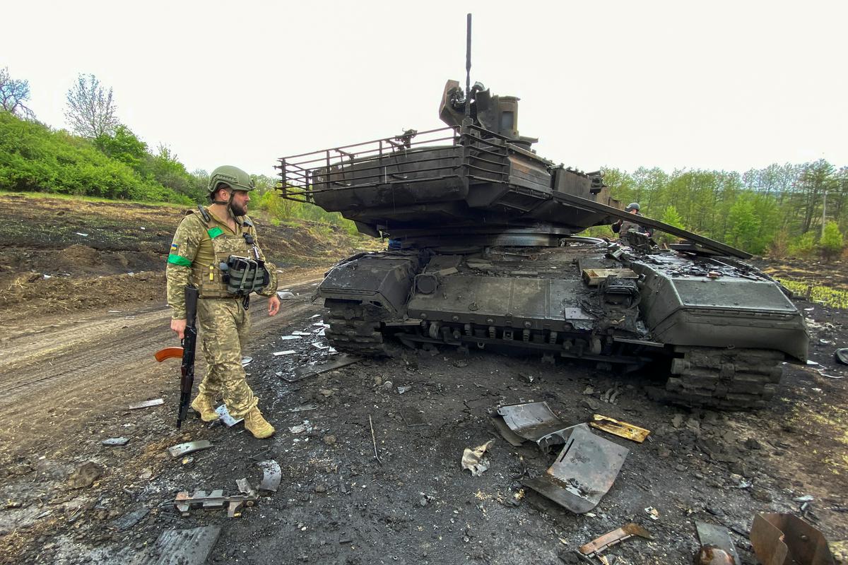 Ukrajinski vojak ob uničenem ruskem tanku v vasi Stari Saltiv v pokrajini Harkov. Foto: Reuters