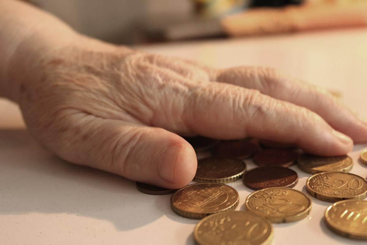 Dlan starejše osebe leži na kovancih na mizi. Foto: Pixabay