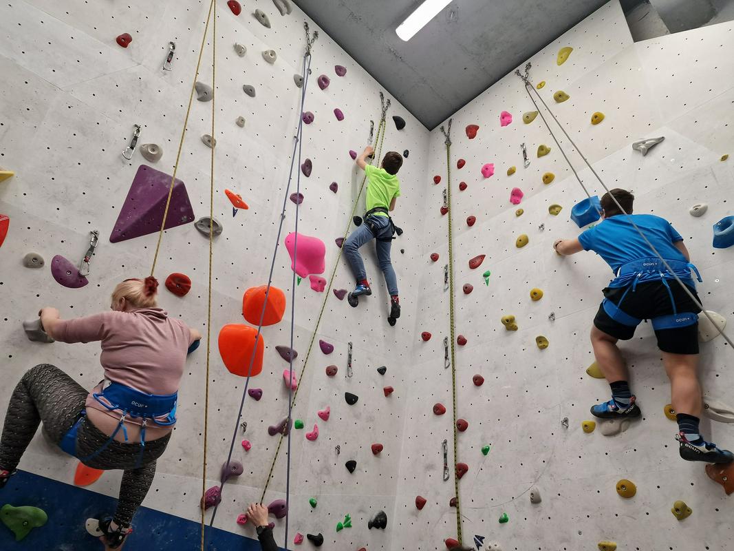 Na fotografiji sta plezalca in plezalka. Trenirajo za pohod na Triglav. Vsi so vpeti v vrvi in plezajo po umetni steni v dvorani. Foto: Center IRIS