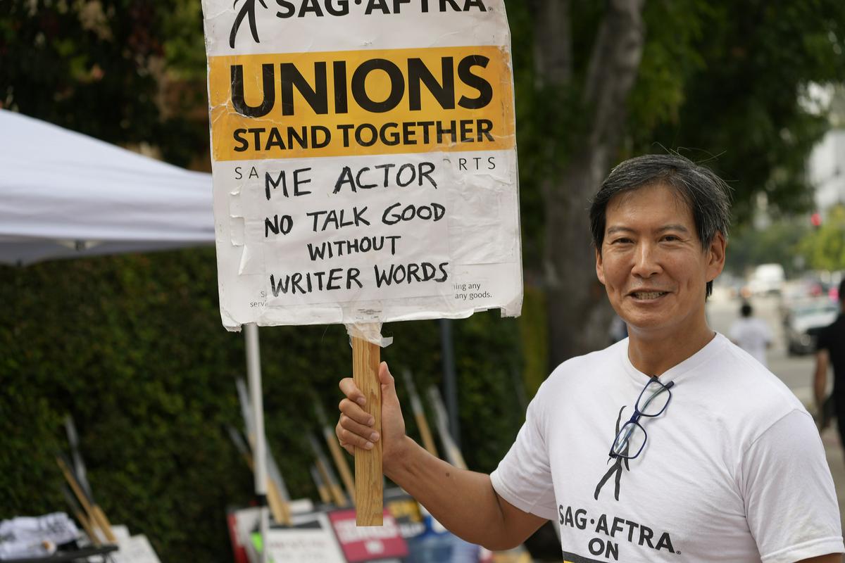 Igralec Vic Chao s transparentom v podporo stavki scenaristov. Igralsko združenje SAG-AFTRA je začelo stavkati 14. julija in ima še več zahtev kot njihovi scenaristični kolegi. Foto: AP