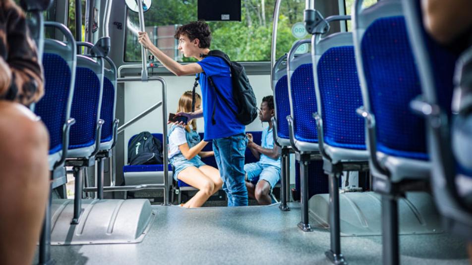 Glavni junak filma Šepet metulja na avtobusu. Stoji in se z roko drži za drog. V ozadju na sedežih sedita dekle in fant. Foto: Constantin Film.Si