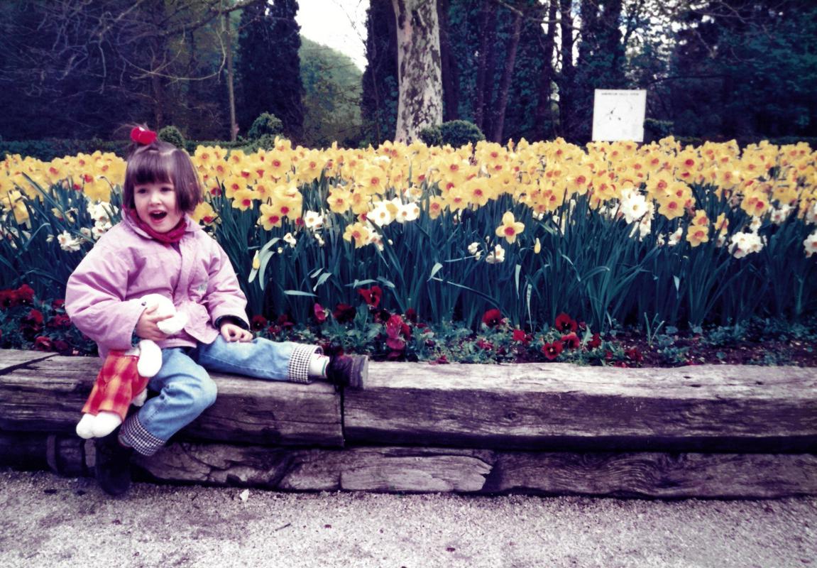 Vanessa stara 4 leta sedi na leseni gredi, ki obdaja nasad rumenih narcis v Arboretumu Volčji Potok. V roki drži belega zajčka in se smeje. Foto: Osebni arhiv