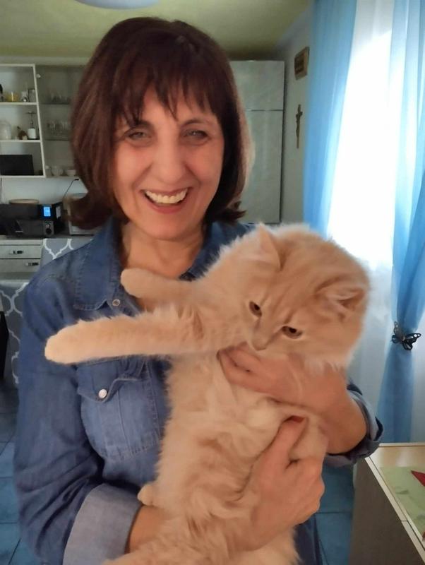 Mirjana s svojim mačkom Majem v naročju. Maj je dolgodak maček z rumenkasto oranžno dlako in zlatimi očmi. Mirjana ga stiska k sebi in se smeji. Foto: MMC RTV SLO/Ana V. Zorman