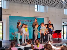 Ajda Smrekar in otroci iz OŠ Poljane na Avdiofestivalu 2025. Foto: Tanja Mojzer
